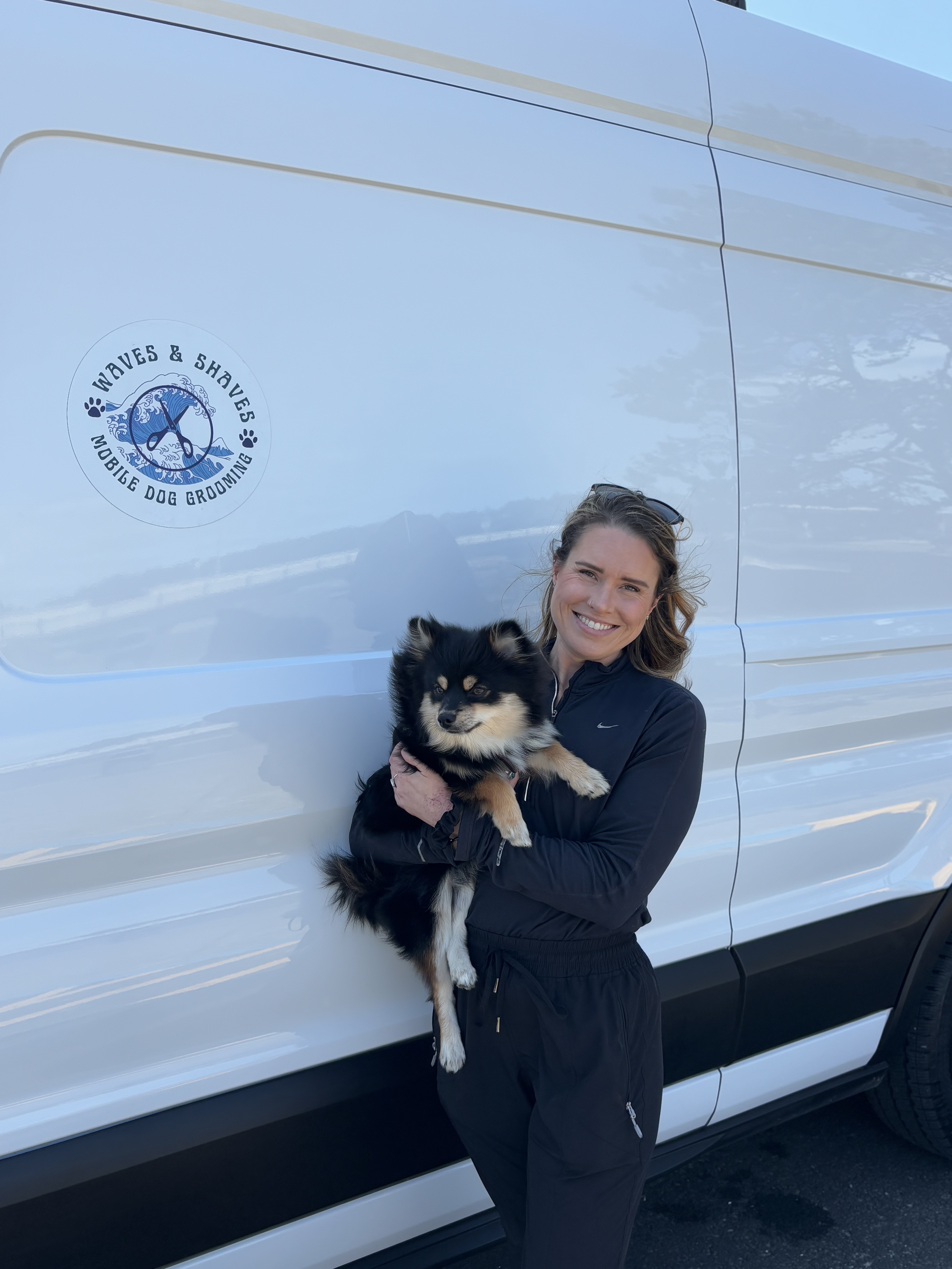 Kelsie, owner of Waves & Shaves Mobile Dog Grooming, holding a dog in front of the grooming van